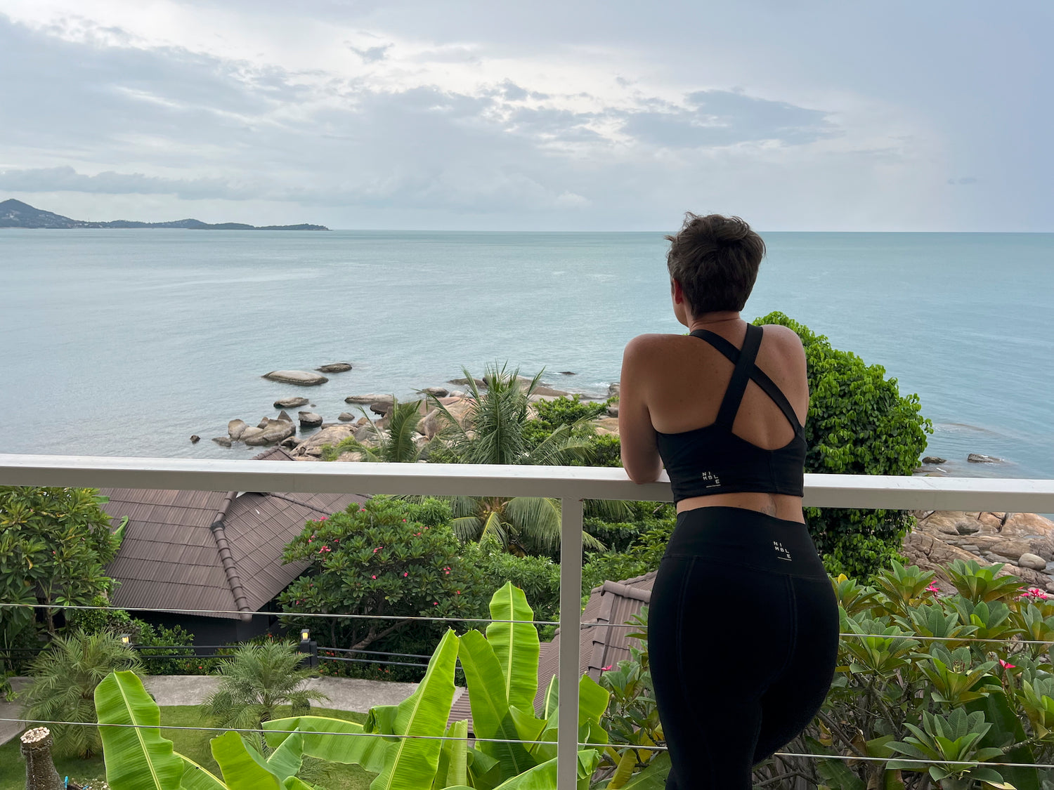 Woman is standing on a balcony overlooking a scenic view of water and rocks.